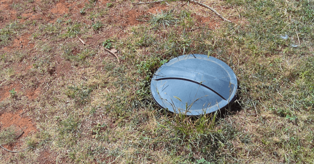 In-ground dog poop digester lid installed in a backyard for pet waste disposal.